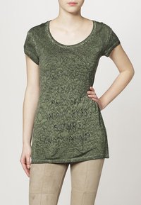 Camiseta verde de manga corta con un patrón texturizado; presenta detalles en texto negro en la parte frontal. Tejido suave, corte relajado.