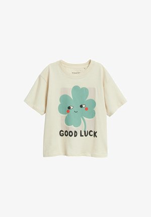 Roomwit T-shirt met korte mouwen en een glimlachende groene klavertjevier afbeelding met de tekst "GOOD LUCK" op de voorkant.