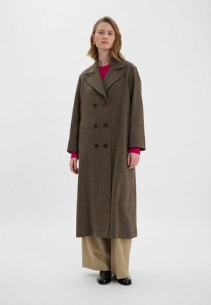 Manteau long en mélange de laine brun avec boutons double boutonnage, col cranté et poches latérales, associé à un haut rose et un pantalon beige.