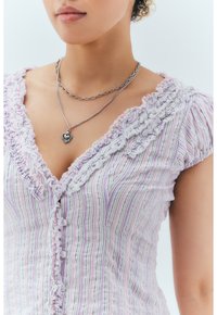 Ljuslila randig blus med krusade kanter, knapp fram, och korta puffärmar; lager av silverhalsband med hjärtformat hänge.