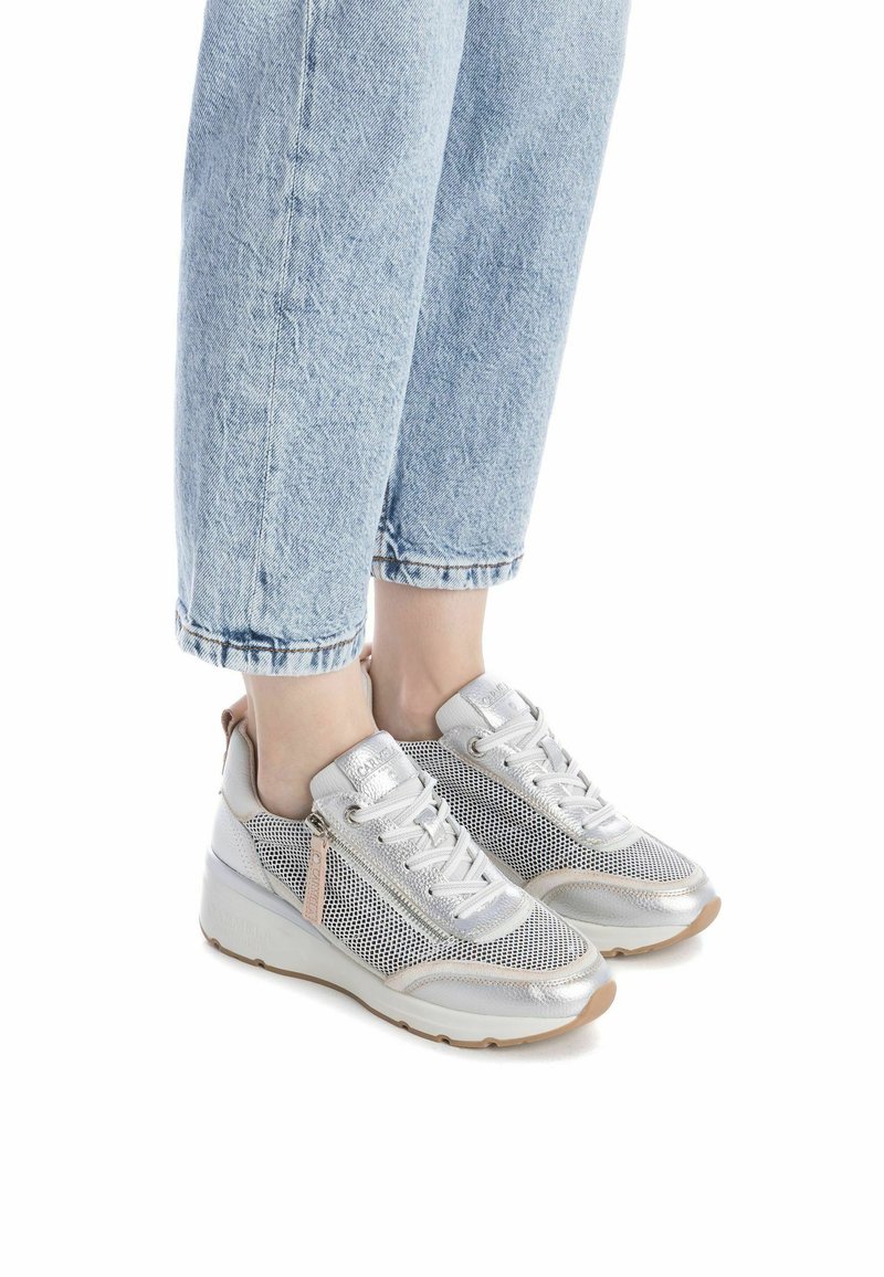 Zapatillas plateadas con malla y detalles metálicos, que presentan un diseño de cordones y cremallera lateral. Suela elevada y puntera redondeada.