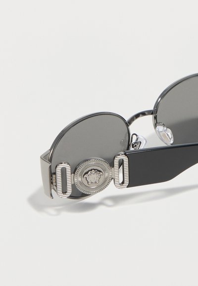 Στρογγυλά γυαλιά ηλίου με σκούρους φακούς και ασημί πλαίσια, διακοσμημένα με ασημένιο μετάλλιο με υφασματικό σχέδιο στο πλαϊνό μπράτσο.