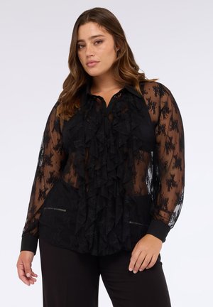 Zwarte semi-transparante blouse met een geplooide voorkant, lange mouwen en zwarte manchetten. Bevat florale kantdetails en verborgen ritsaccenten.