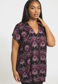 Czarna tunika z żywym różowym wzorem kwiatowym, zaprojektowana w dekolt w kształcie litery V, z krótkimi rękawami i luźnym krojem. Miękka, lekka tekstura materiału.