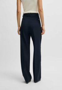 Pantaloni larghi a vita alta di colore blu navy, realizzati in tessuto testurizzato. Presentano passanti per cintura e una piccola etichetta con il marchio sul retro.