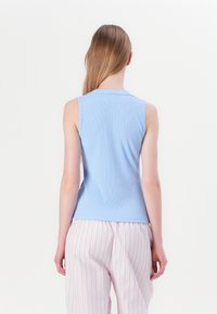 Top de tirantes de canalé azul claro con escote redondo y diseño sin mangas, combinado con pantalones holgados a rayas rosas y blancas.
