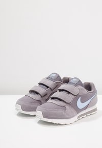 Grå träningsskor med kardborreband, i mocka och mesh-material, vit sula, ljusblå Nike-logotyp och vadderad ankel för komfort.