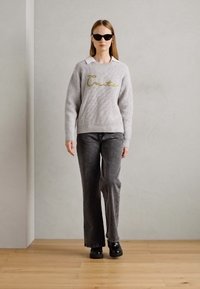 Gray knitted sweater with a crew neckline, featuring green embroidered text. Paired with dark gray flared jeans and black footwear.