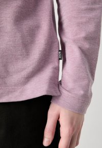 Košulja dugih rukava u svijetlopurple tkanini. Ima okrugli izrez i malu crnu oznaku brenda na donjem šavu. Detalj s teksturiranim tkanjem.