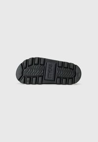 Svart gummisåle med et teksturert mønster som har spor og rygger for godt grep. Sentralt logo preget i rektangulært område.