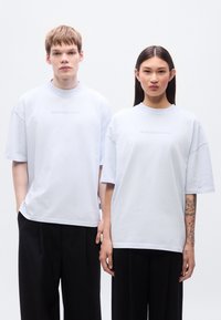 Φαρδιά γαλάζια μπλουζάκια από απαλό ύφασμα, με διακριτική εκτύπωση κειμένου, συνδυασμένα με μαύρο παντελόνι φαρδιά γραμμή.