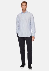 Light blue striped long-sleeve shirt, button-down front, soft fabric. Paired with dark pants and black sneakers, standing against a plain background.