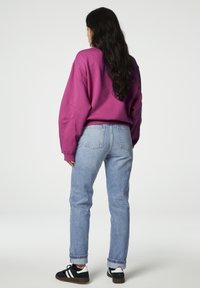 Felpa viola oversize, jeans in denim azzurro con risvolti, e sneaker nere con dettagli bianchi. Tessuto di texture liscia.