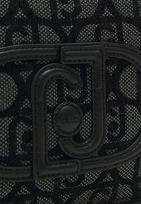 Borsa a tracolla in tessuto nero a motivi, dotata di un distintivo hardware in pelle nera con dettagli in logo stampato e una finitura testurizzata.