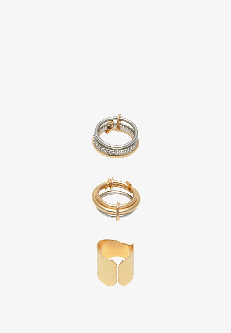 Három gyűrű készlet: egy ezüst, világos kövekkel, egy arany és egy arany, nyitott mandzsettagyűrű. Simai textúra, változatos formák, fényes fémes felület.