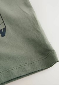 Nahaufnahme eines gefalteten grünen T-Shirts, das seine Textur und den genähten Saum zeigt, mit einem subtilen Design, das auf legere Kleidung hinweist.