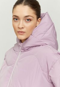 Light purple puffer jacket with a high collar and hood. Features a front zipper and stitched pattern detailing on the body.