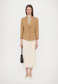 Lys brun lin blazer med notched lapels, parret med en krämfarvet hæklede midi-skjørt. En sort vævet håndtaske og lyse sko fuldender looket.