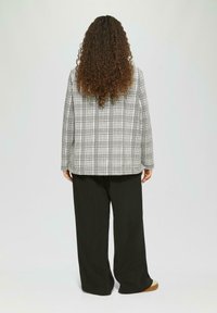 Karierter Blazer in Schwarz und Weiß, mit lockerer Passform und geradem Schnitt. Kombiniert mit weiten schwarzen Hosen.