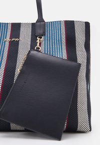 Vävd tygväska med blå, röda och vita ränder, kompletterad med en avtagbar svart läderpouch med präglad logotyp.