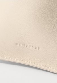 Materiale in pelle beige con una superficie testurizzata, con marchio in rilievo "BONASTRE" e un sottile dettaglio di cucitura lungo il bordo.