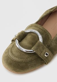 Mocasín de ante verde oliva con hebilla redonda de plata y detalle de correa, con detalles cosidos y un interior de cuero liso.