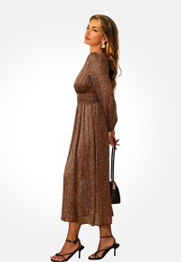 Brązowa kwiatowa sukienka midi z długimi rękawami, zaznaczoną talią i plisowanym dołem. Połączona z czarnymi sandałami na paski i małą torebką.
