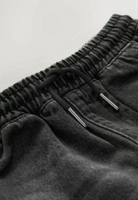Pantaloni sport din denim negru cu talie elastică, șnur de ajustare și accente metalice, care evidențiază o textură moale și o croială lejeră.