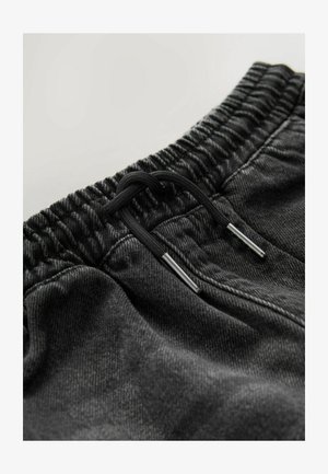 Crne traper hlače trenerke imaju elastični pojas s vezicom i metalnim detaljima, pokazujući mekanu teksturu i ležeran kroj.