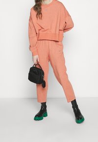 Coral sweatshirt and matching pants in soft fabric, featuring a cropped design. Black handbag with a round accent and chunky green platform boots.