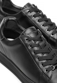 Sneakers in pelle nera con punta rotonda, lacci neri piatti, occhielli argentati e suola in gomma testurizzata. Logo impresso sulla linguetta.