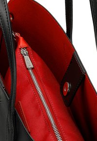 Černá kabelka s červeným vnitřkem. Obsahuje zipovou kapsu s kovovými prvky a patentním zapínáním. Hladký kožený povrch a textilní podšívka.