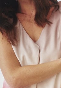 Haut sans manches rose clair avec un design en V. Texture lisse et dégradé de couleur subtil. Bras visible, mettant en valeur le teint et les détails fins.