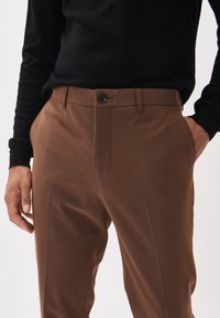 Bruna skräddarsydda byxor med en slät yta, med knappstängning, framfickor och en slim fit-design. Tillsammans med en svart topp.