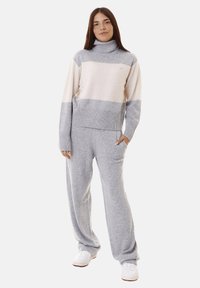 Maglione a righe grigio chiaro e crema con colletto alto, polsini a costine e pantaloni ampi grigi abbinati. Tessuto a maglia morbido; design casual.