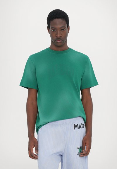 T-shirt verde a girocollo realizzata in tessuto morbido, con maniche corte e una vestibilità comoda, abbinata a pantaloni a righe chiare.