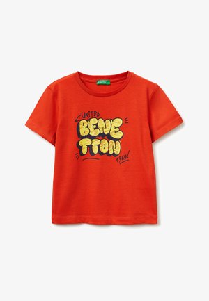 Rood T-shirt met korte mouwen met gele en zwarte graffiti-stijl tekst "United Benetton 1965" op de voorkant en een groen merklabel aan de binnenkant van de kraag.