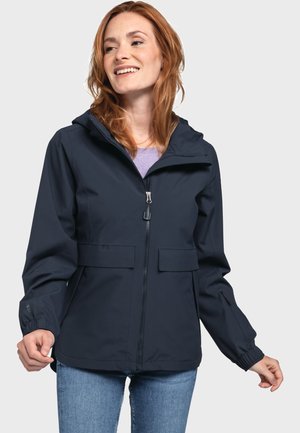 Marineblauer wasserdichter Jacke mit Kapuze, Reißverschluss, zwei Fronttaschen, elastischen Bündchen und lässigem Schnitt, getragen über einem lavendelfarbenen Oberteil.