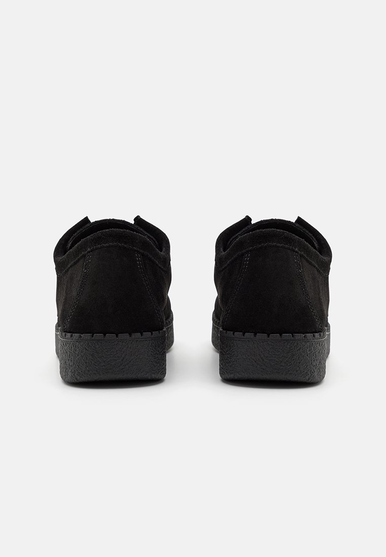Chaussures en suède noir avec une finition texturée, présentant une semelle en caoutchouc noir et un design minimaliste sans quincaillerie ou accents visibles.