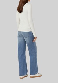 Witte langmouwige geribbelde top gecombineerd met losse blauwe denim jeans. Sneakers hebben een witte bovenkant en een gumkleurige zool. Minimalistisch ontwerp, casual fit.