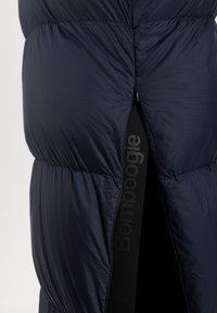 Marine pufferjas met een gestructureerde afwerking, met een opvallende ritsopening en een zwarte elastische band met de tekst "Bombogie" langs de naad.