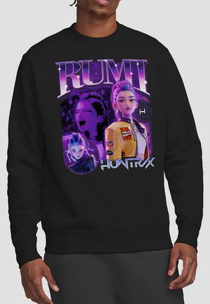 Schwarzer Kapuzenpullover mit lebhaftem lila und gelbem Grafiken einer animierten Frau in einer gelben Jacke, fett gedruckter "RUMI"-Text oben und "HUNTRX" unten den Bildern.
