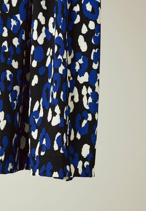 Tissu noir à la surface texturée arborant un imprimé léopard abstrait avec des taches bleues et blanches. Détail visible des bords du tissu et de la couture.