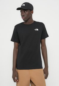 Μαύρο βαμβακερό t-shirt με κοντά μανίκια και στρογγυλή λαιμόκοψη, με μικρό λευκό λογότυπο στο αριστερό στήθος. Συνδυασμένο με καφέ παντελόνι και καπέλο στο ίδιο χρώμα.