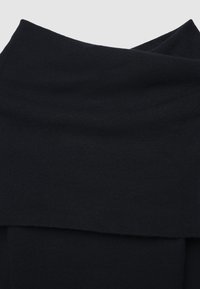 Tessuto a maglia nera a coste piegato nella parte superiore, che mostra la texture e il materiale morbido e elastico.