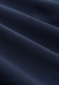 Tmavě modrá textilie s texturovaným, pevně tkaným vzorem, vystavená v jemných záhybech.