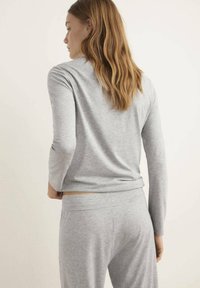 Grå långärmad tröja i mjukt material parat med matchande byxor. Tyget är slätt med en avslappnad passform och enkel design.