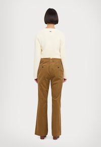 Pulover crem cu dungi, cu decolteu rotund și un mic logo pe spate, asortat cu pantaloni evazați din catifea de culoare maro, cu buzunare la spate.