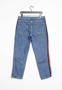 Vaqueros de mezclilla azul con un corte relajado, con franjas laterales rojas y negras, cinco bolsillos y un diseño de pierna recta, colgando de una percha negra.