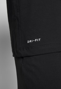 Musta Dri-Fit urheilupaita, lyhythihainen, sisältää pehmeän, hengittävän kankaan. 'DRI-FIT' -merkintä valkoisena helmassa. Saumayksityiskohta näkyvissä.